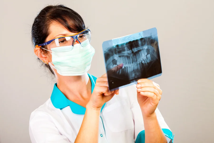 Dental professional in mask reviewing a panoramic X-ray film
